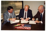 Three men signing documents